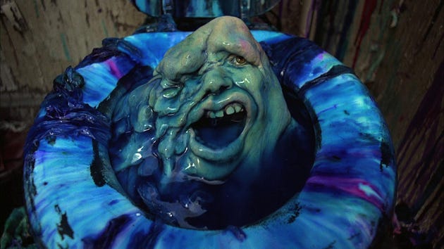 A grotesque creature with a face emerging from a brightly colored toilet bowl, featuring blue and purple hues and exaggerated facial features.