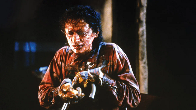 A man with disfigured skin and a pained expression holding a yellow object in a dimly lit setting, wearing a tattered shirt.
